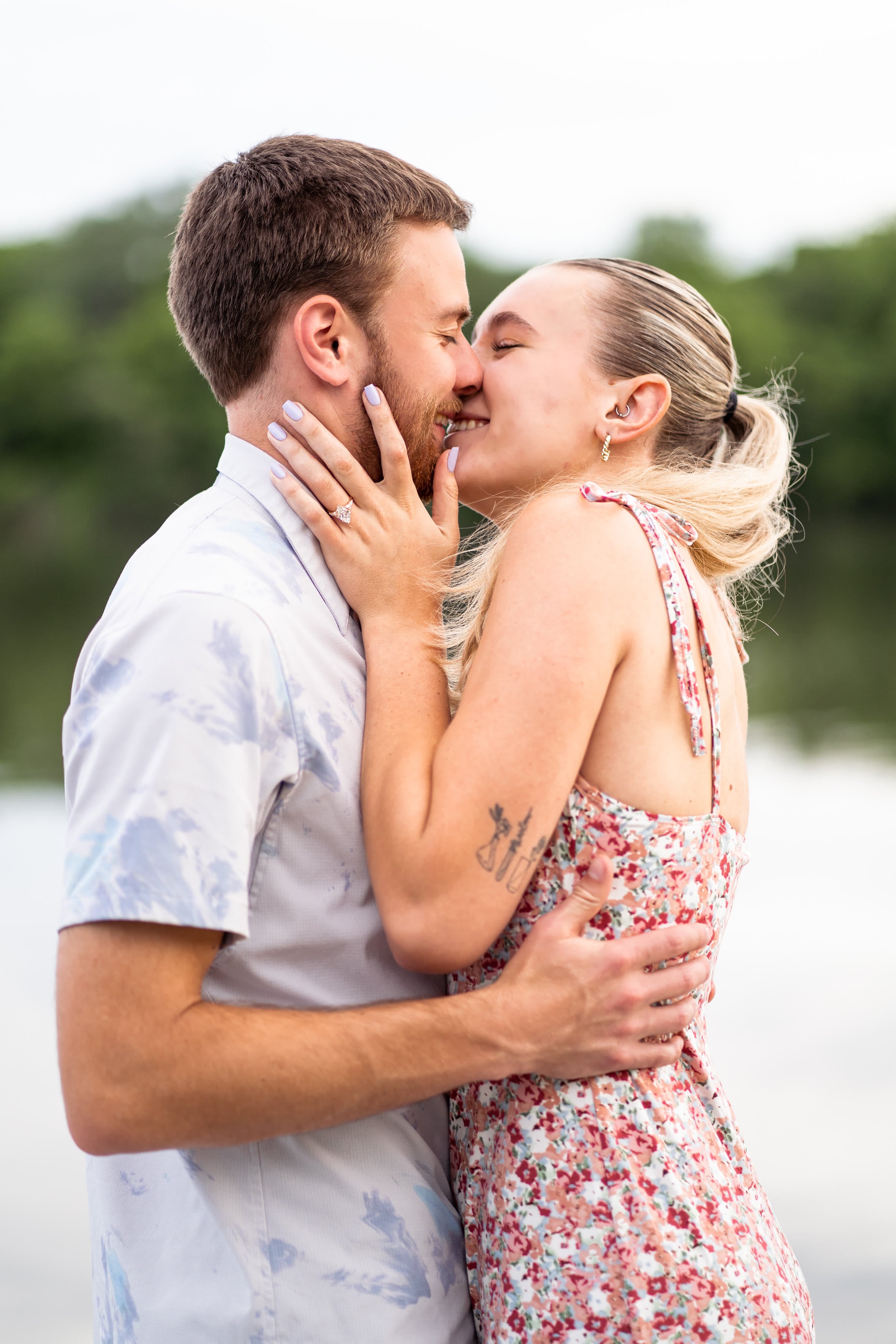 Engaged couple kissing beside a lake